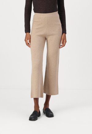 Pantalons en tricot beiges avec un design à jambes larges, une taille haute et une texture douce. Associés à des mocassins noirs.
