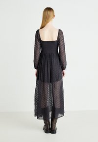 Czarna maxi sukienka z długimi, przezroczystymi rękawami, marszczonym biustem oraz tkaniną w gwiazdy, z luźnym krojem sięgającym kostek.