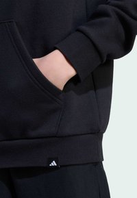 Black sweatshirt with a front pocket, ribbed cuffs, and hem. Features a small white Adidas logo tag at the bottom left.