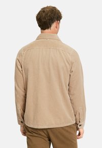 Braunes Cordhemd mit vertikalen Streifen, Knopfmanschetten und einem Kragen. Der Stoff hat eine strukturierte Oberfläche. Verfügt über ein Detail am Rücken.