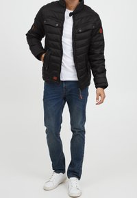Zwarte gevoerde jas met drukknoopjes en twee borstzakken. Draag het over een witte t-shirt, in combinatie met blauwe jeans en witte sneakers.