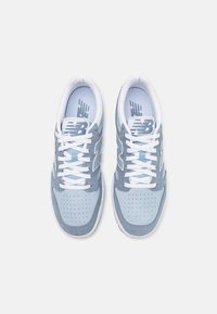 Hellblaue Sportschuhe aus Wildleder und Mesh-Materialien, weiße Schnürsenkel, durchbrochene Struktur und ein größeres "N"-Logo an den Seiten.