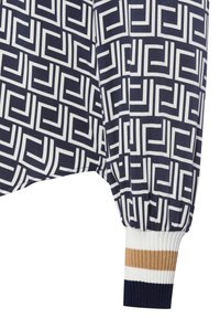 Maglietta a maniche lunghe in blu navy e bianco con motivo geometrico, caratterizzata da polsini a coste con strisce dorate, bianche e blu navy. Tessuto morbido con una consistenza liscia.