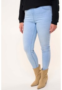 Jean skinny bleu clair avec une texture lisse et un léger dégradé, associés à des bottines beiges à bout pointu et tige effilée.