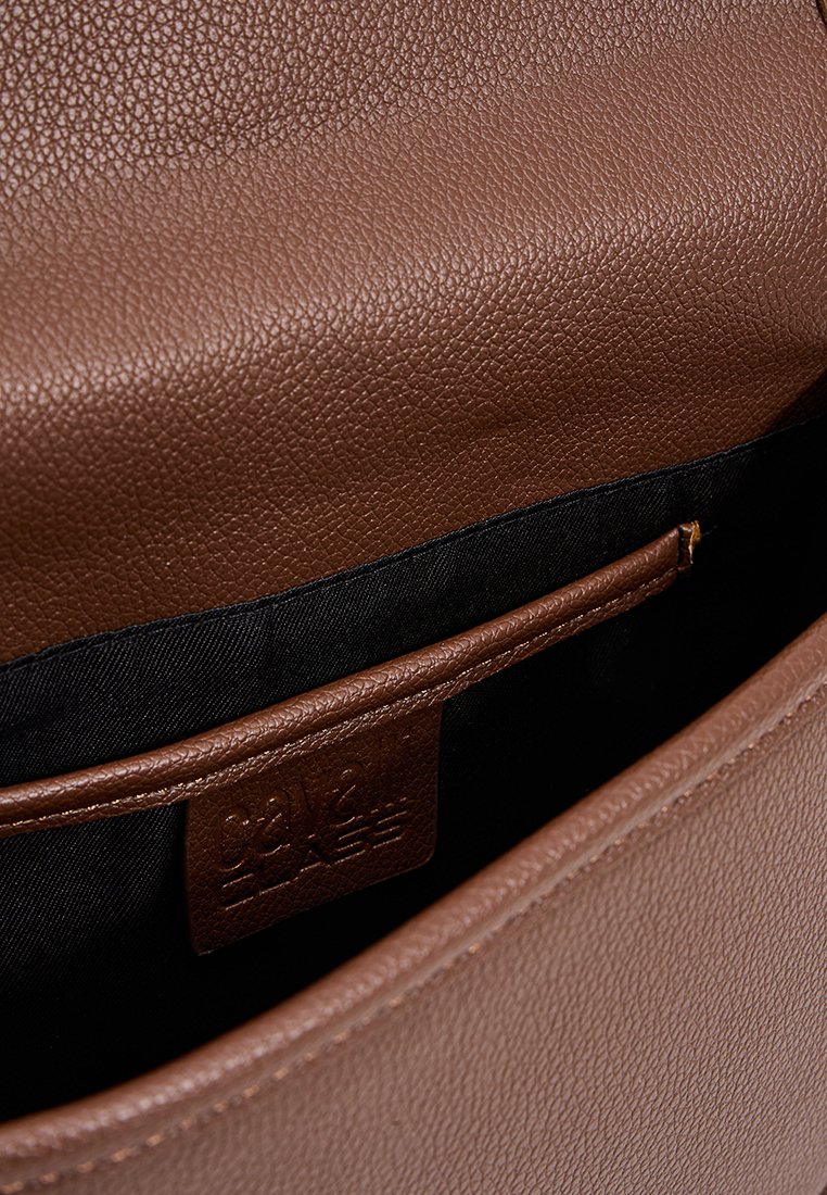 Bolso de mano de cuero marrón con un exterior texturizado, un forro de tela negra y un bolsillo interior con una etiqueta de logo.