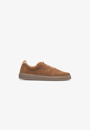 Brown suede sneaker with lace-up design, rounded toe, and a textured rubber sole. Features a smooth leather accent at the heel.