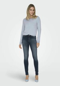 Helles blaues Langarmoberteil, figurbetonte dunkelblaue Skinny Jeans und hellblaue High Heels. Glattes Material mit minimalen Akzenten und einem klassischen Design.