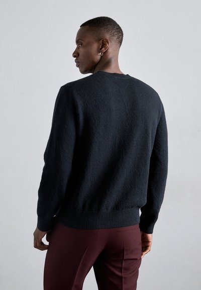 Μαύρος πλεκτός σκούφος με υφή, στρογγυλή λαιμόκοψη και ριμπ μανίκια και τελείωμα, σε συνδυασμό με μαρόν παντελόνι.