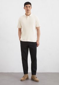 Jasna kremowa polo z prążkowanej tkaniny, krótki rękaw, w połączeniu z czarnymi, dopasowanymi spodniami oraz beżowymi butami na sznurówki. Minimalistyczny design, brak wzorów.