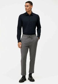 Camicia blu navy con bottoni abbinata a pantaloni jogger grigi, aderenti, con vita elasticizzata. L'outfit è completato da scarpe nere.