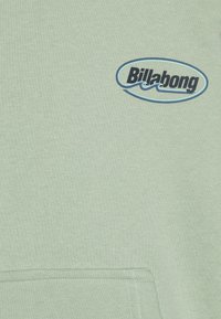 Light green hoodie made from soft fabric features a blue Billabong logo on the chest and a kangaroo pocket at the front.
