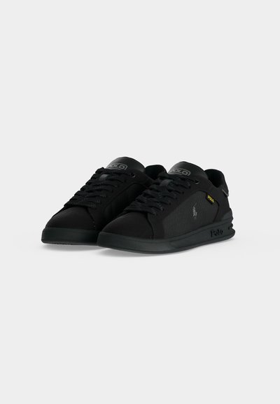 Ζευγάρι μαύρα low-top αθλητικά παπούτσια Polo Ralph Lauren με λογότυπο στη γλώσσα, πλευρικό λογότυπο και μαύρα κορδόνια σε απλό φωτεινό φόντο.