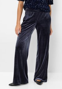 Pantalon à jambes larges en velours bleu marine, doté d'une taille élastique et d'une texture lisse. Associé à des ballerines noires à bout pointu.