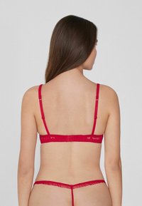 Červený krajkový set spodního prádla, který zahrnuje podprsenku s nastavitelnými popruhy a zapínáním na háček, doplněnou o odpovídající tanga s volánkovými detaily.