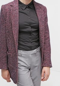 Blazer texturizado en color burdeos con una silueta estructurada, usado sobre una camisa negra con botones y pantalones grises a medida. Bolsillos parche destacados.