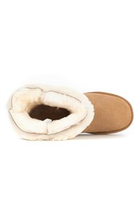 Brun mocka stövel med en fluffig vit pälsfoder, rund form och sydda dekorationer runt öppningen. Texturerad yta.