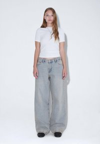 Ljusblå, oversized denimjeans med en urblekt yta, kombinerat med en figurnära vit t-shirt. Tyget verkar mjukt med en slät textur.