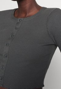 Mörkgrå ribbad cardigan med rund halsringning, knappstängning och en kortad nederkant med rå kantdetaljer.