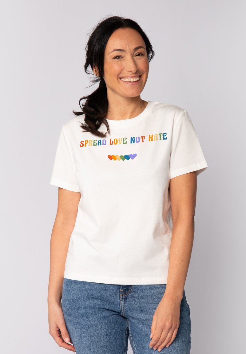 Witte katoenen t-shirt met de tekst "SPREAD LOVE NOT HATE" in kleurrijke letters, met daaronder een regenbooghart grafiek. Korte mouwen en ronde hals.