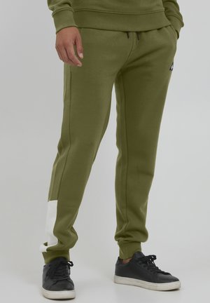 Olivegrønne joggebukser med slim fit, med en hvit kant nede på venstre ben og snøring i livet. Blandingsmateriale av bomull.