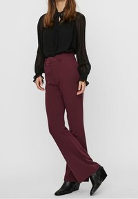 Bordeaux brede pijpenbroek met een getailleerde pasvorm, gecombineerd met een zwarte sheer blouse met lange mouwen. De outfit wordt afgemaakt met zwarte enkellaarsjes met hak.