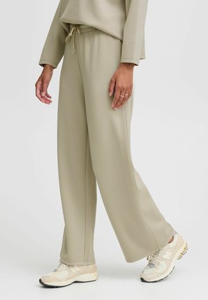 Person wearing beige wide-leg pants and a matching top with cream and gray sneakers, standing against a plain background.