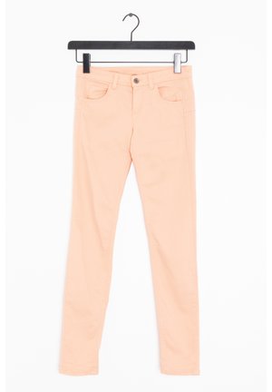 Licht perzikkleurige slim-fit broek die aan een zwarte hanger hangt tegen een witte achtergrond, met zichtbare knoop en voorzakken.