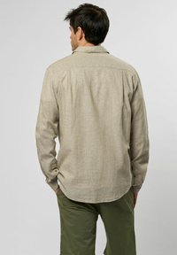 Beige overhemd met lange mouwen, gemaakt van een textuurstof, voorzien van een knoopsluiting bij de manchetten en een detail op de achterkant, met een gebogen zoom.