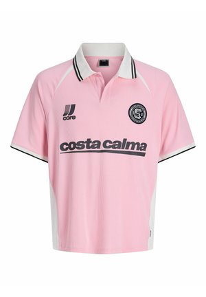 Dreng står frontalt iført en lyserød polo-shirt med sort tekst, lyse denimshorts, hvide sokker og sort-hvide sneakers på en hvid baggrund.