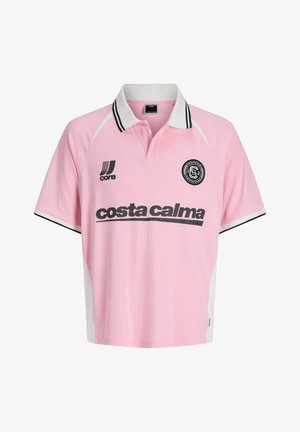 Ragazzo in piedi di fronte, indossa una polo rosa con scritte nere, pantaloncini in denim chiaro, calzini bianchi e sneaker bianco-neri su sfondo bianco.