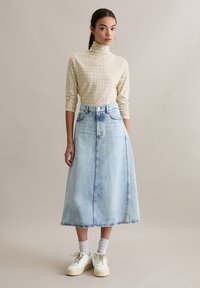 Beżowo-brązowy golf w kratę połączony z jasnoniebieską długą spódnicą jeansową o wysokim stanie i przednich kieszeniach. Białe trampki i skarpetki.