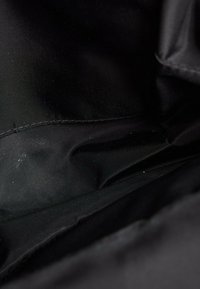Gros plan d’un tissu noir lisse avec des coutures et plis visibles, montrant la texture et des reflets subtils de lumière.