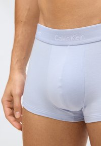 Světlé modré bavlněné boxery s měkkým elastickým pasem, na kterém je bílé logo "Calvin Klein". Hladká textura a těsný střih.