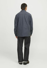 Mörkblå skjorta med knappar och krage, avslappnad passform, långa ärmar och bakstycke med detalj, kombinerad med mörka jeans och svarta skor.