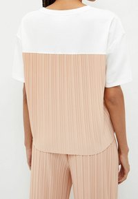 Farveblokeret t-shirt med en hvid øverste sektion og en plisseret ferskenfarvet nederste sektion. Blødt stof med en løs pasform og rund kant.