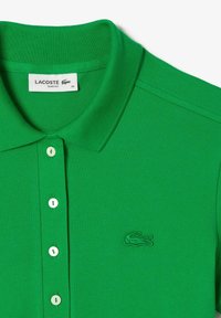 Grön, slim-fit polo skjorta gjord av strukturerad tyg. Har en klassisk krage, tre vita knappar och en broderad logotyp på bröstet.