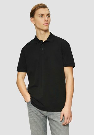 Zwarte poloshirt van katoen, met een kraag, een drieknoopsluiting en korte mouwen. Gecombineerd met lichtgrijze jeans.