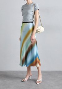 Haut à manches courtes côtelé gris clair associé à une jupe en satin fluide avec un motif bleu et vert. Comprend des sandales à talons blancs et un sac beige.