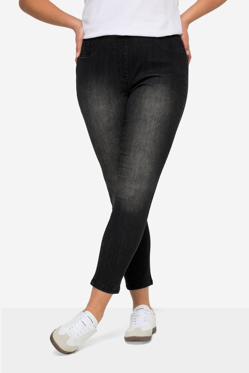 Persoon die vervaagde zwarte skinny jeans en witte sneakers draagt, staand met gekruiste benen en handen in de heupen.