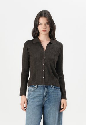 Bruine geribbelde cardigan met lange mouwen, een kraag en sluiting met parelknoopjes, gecombineerd met lichtblauwe wijde spijkerbroeken.