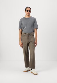 Gray short-sleeve t-shirt paired with loose, light brown jeans and white sneakers. The sunglasses add a round, dark accent.
