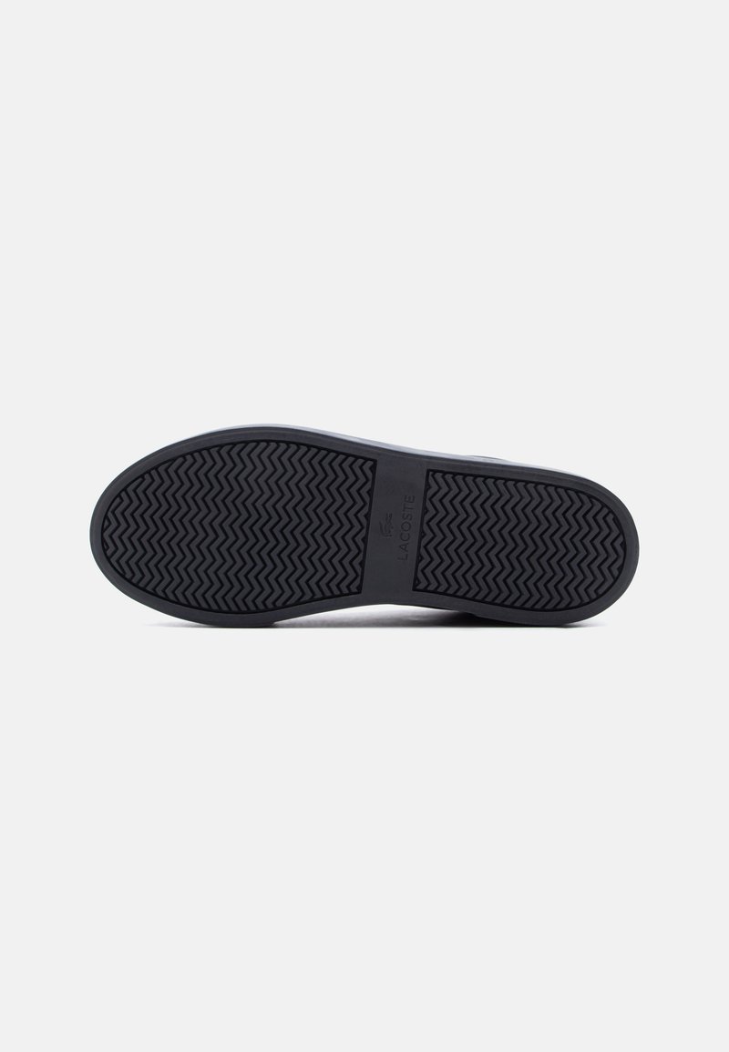 Zool van een zwarte Lacoste-schoen met een visgraatprofiel en het Lacoste-logo op een witte achtergrond.