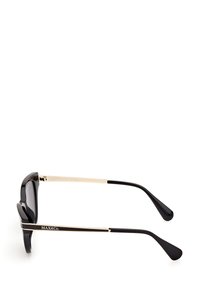 Gafas de sol negras con montura de gran tamaño, detalles en metal dorado en las patillas y puntas curvadas en negro. Las lentes tienen un tinte oscuro y un acabado brillante.