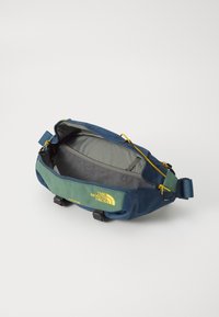 Borsa a vita leggera blu e verde con zip gialla, logo frontale e tasca interna in rete. Design compatto con tracolla regolabile.