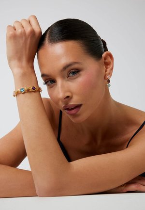 Bracciale in oro con pietre multicolori, forme rotonde, texture liscia. Gli orecchini abbinano il design del bracciale con uno schema cromatico simile.