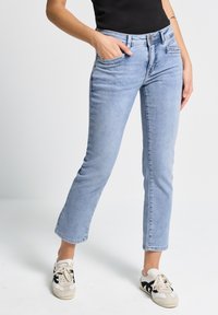 Jeans de mezclilla azul claro con corte recto, cinco bolsillos y cremallera. Presentan un desvanecimiento sutil y detalles de hardware mínimos.