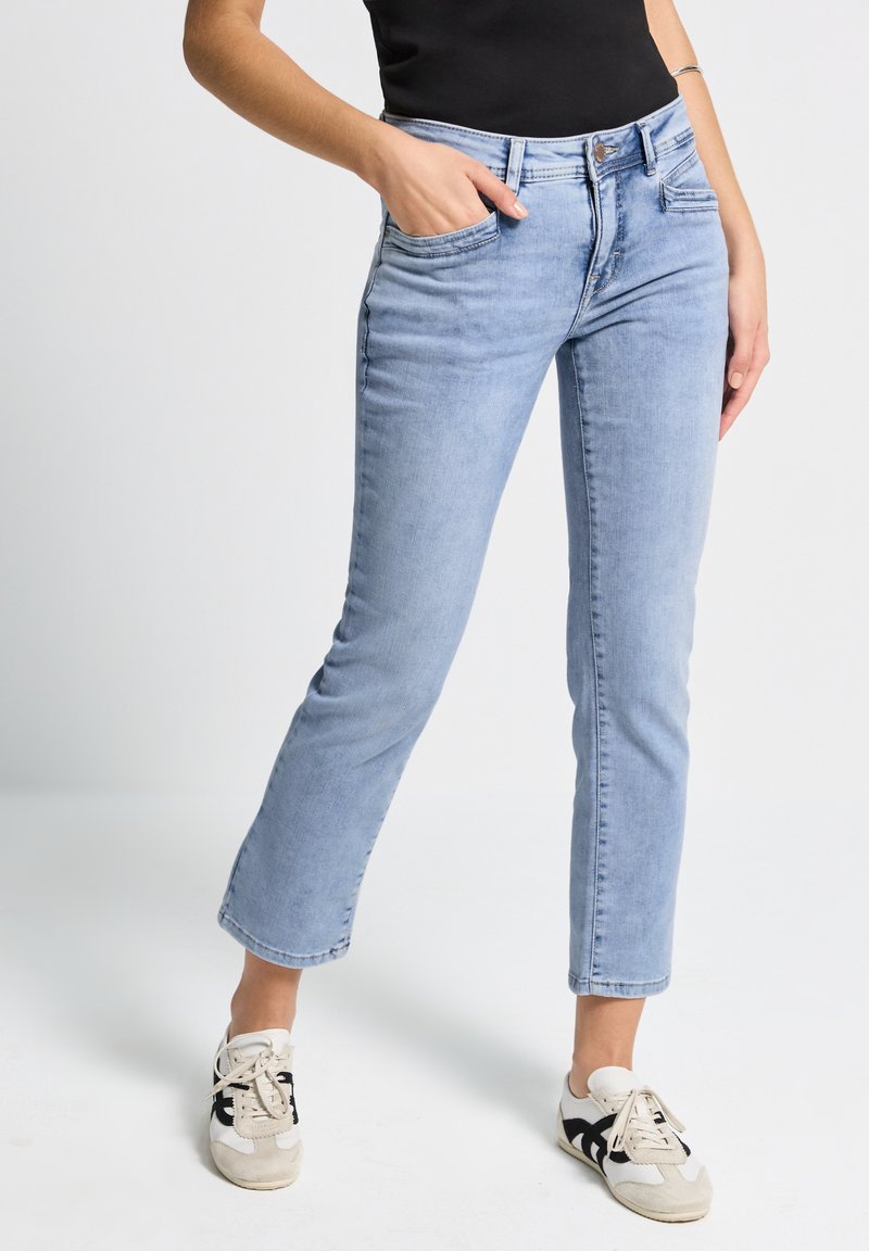 Jeans de mezclilla azul claro con corte recto, cinco bolsillos y cremallera. Presentan un desvanecimiento sutil y detalles de hardware mínimos.