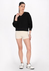 Svart kort ärmad tröja med v-ringning, kombinerad med beige shorts. Modellen bär vita sneakers och silverörhängen i form av ringar. Släta texturer.