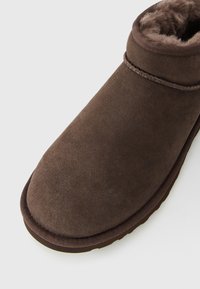Brown suede ankle boot with soft fur lining and stitched trim on a white background.