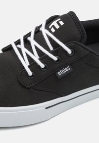 Fekete vászon gördeszkás cipők halszálka mintával, fehér fűzőkkel és fehér gumitalppal. Az oldalán "etnies" logó található.